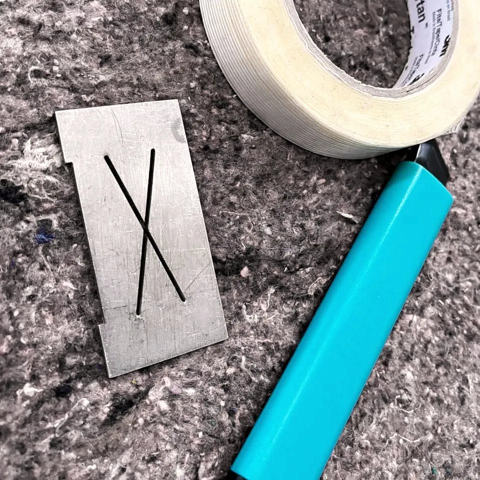 Gabarito com fenda em X, estilete e rolo de fita usados no teste de aderência