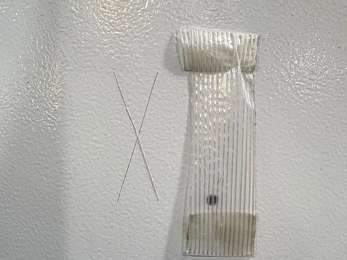 Corte em X sem desplacamento em pintura cinza texturizada e, ao lado, a fita retirada do corte, sem tinta aderida