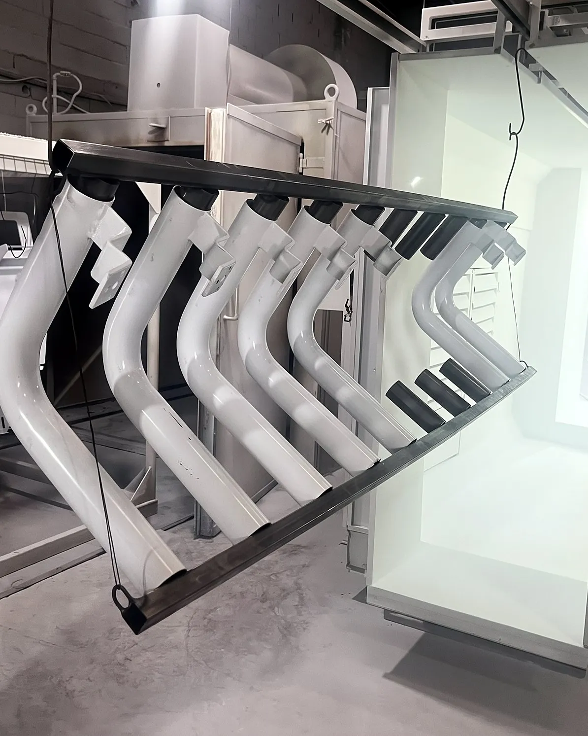 Peças brancas de formato curvo penduradas na cabine de pintura