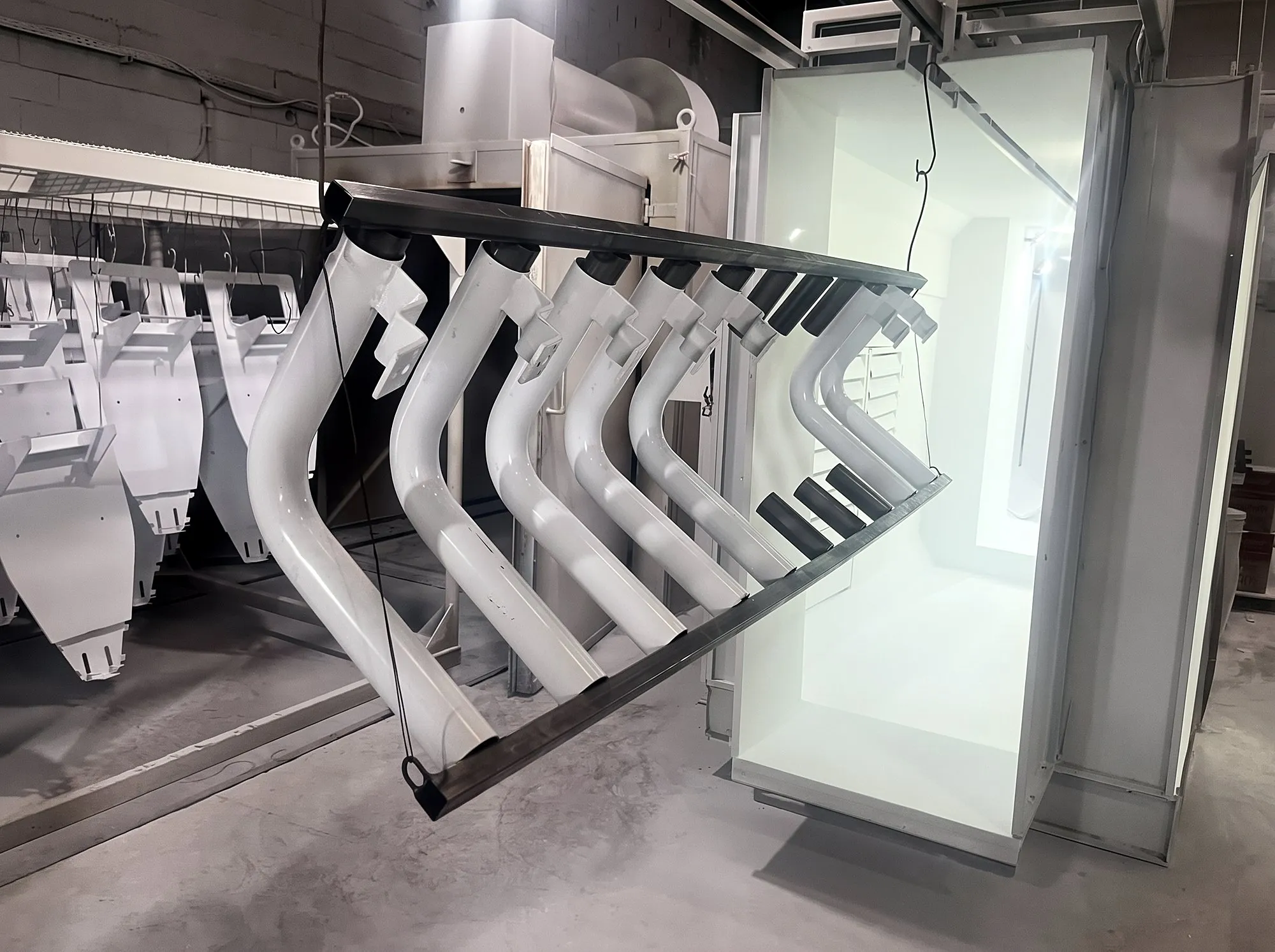 Peças brancas de formato curvo penduradas na cabine de pintura