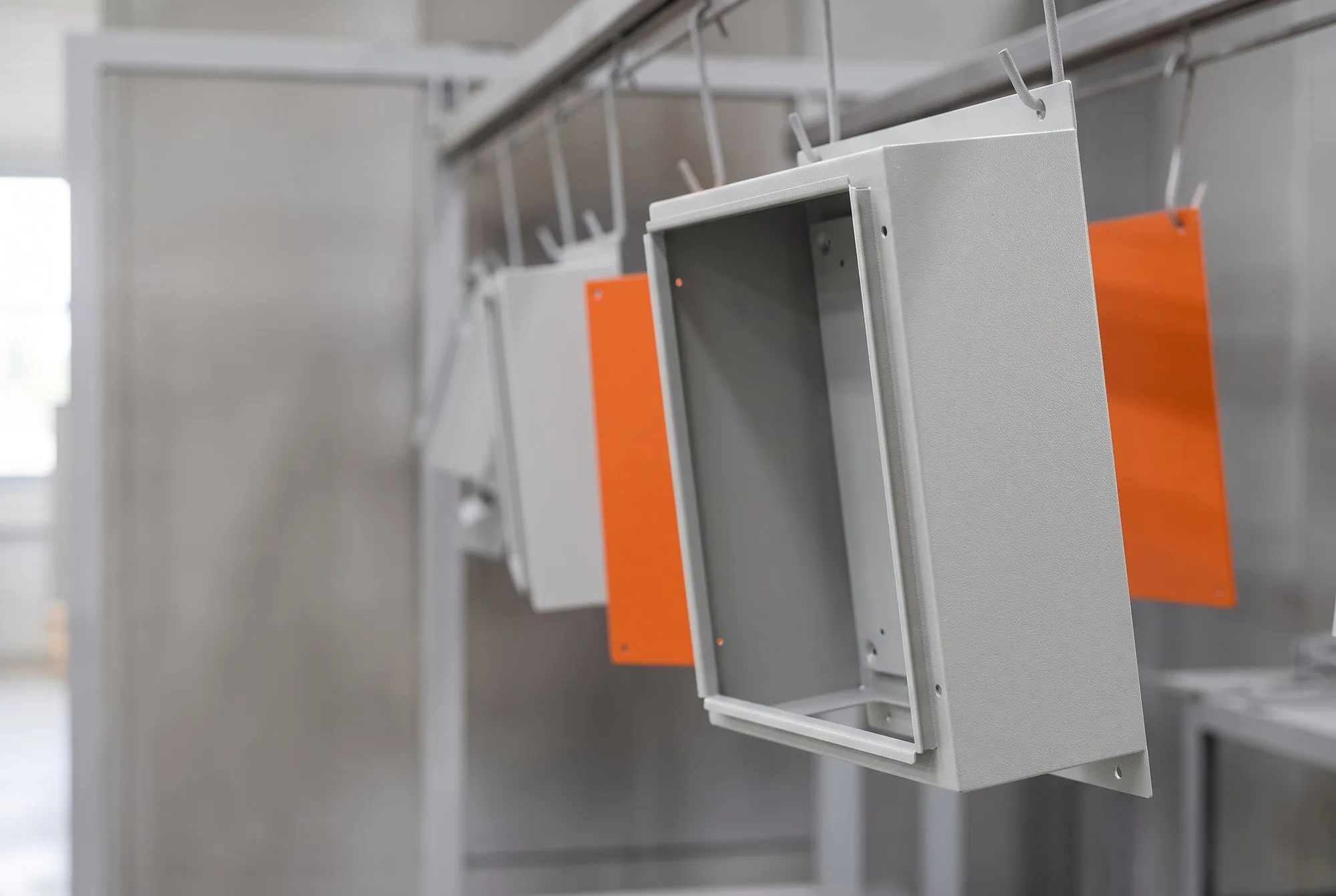 Gabinete de painel elétrico em cinza RAL 7035 texturizado e placas de montagem laranja penduradas na linha de pintura