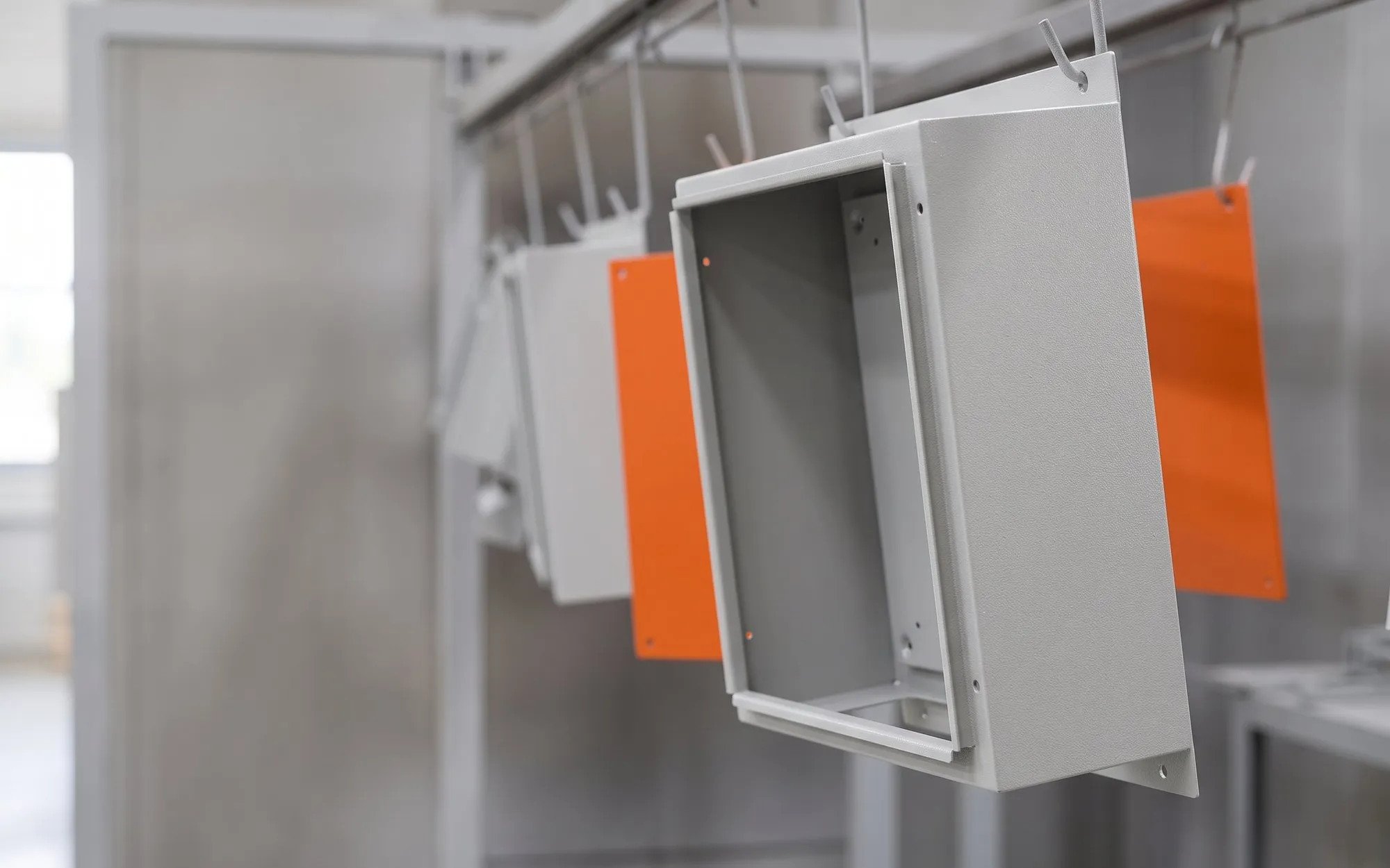 Gabinete de painel elétrico em cinza RAL 7035 texturizado e placas de montagem laranja penduradas na linha de pintura