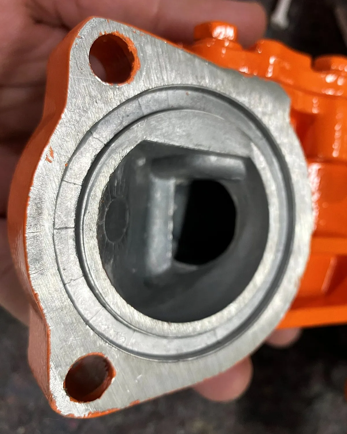 Peça fundida pintada em laranja, com a face usinada do flange protegida e sem tinta