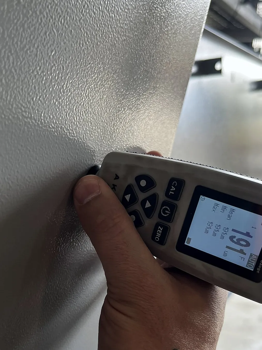 Medição de camada em peça cinza pendurada na linha, leitura de 191 µm em sistema de duas demãos