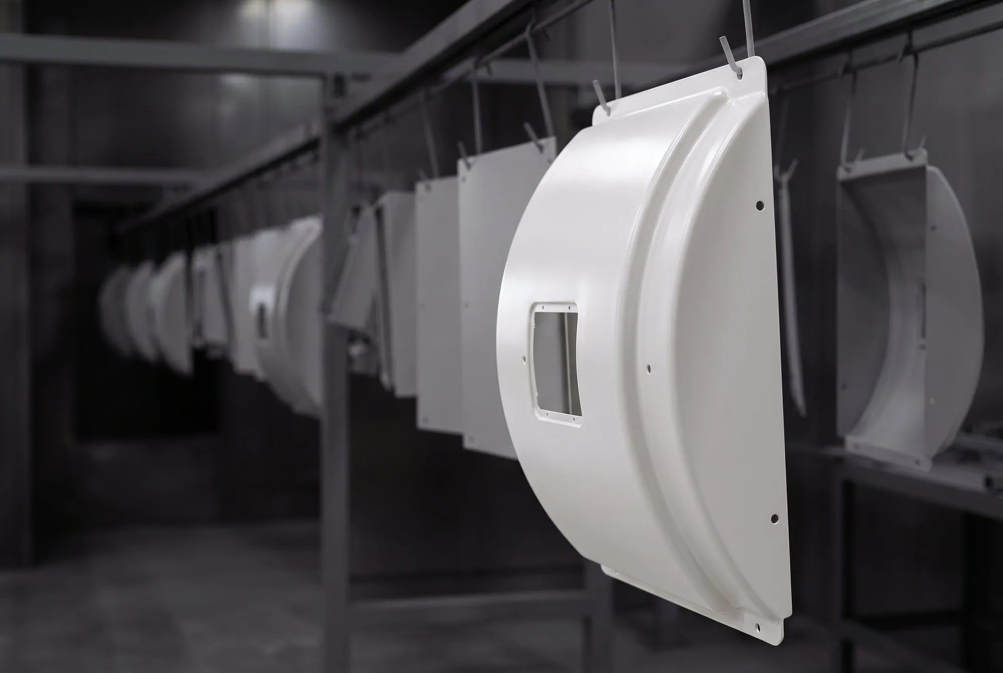 Carenagem branca de equipamento de diagnóstico por imagem pendurada na linha de pintura, com outras peças do lote ao fundo